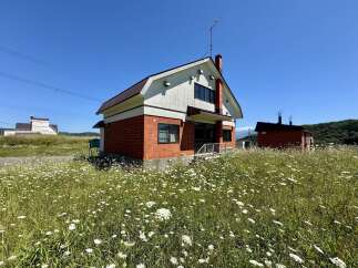 Charming brick house nestled in a field of wildflowers under a clear blue sky.
