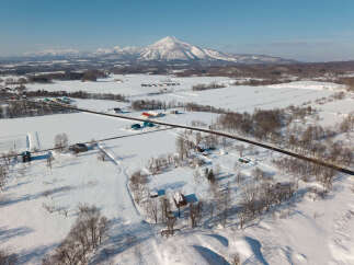 Discover serene winter living in this picturesque landscape, featuring charming homes nestled amidst snow-covered fields and a majestic mountain backdrop.
