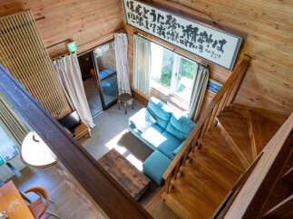 Experience cozy living in this charming wooden cabin, featuring a spacious living area with a comfortable blue sectional sofa bathed in natural light.