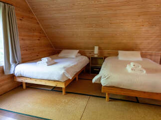 Experience cozy comfort in this charming wooden cabin bedroom, featuring two twin beds with crisp white linens and neatly folded towels.