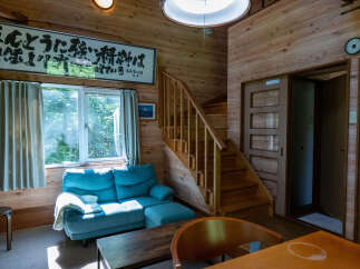 Experience cozy living in this charming wooden cabin, featuring a comfortable blue sofa and a unique staircase leading to the upper level.