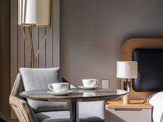 Experience comfort and style in this inviting hotel room, featuring a cozy seating area with two chairs and a marble-top table, perfect for enjoying morning coffee.