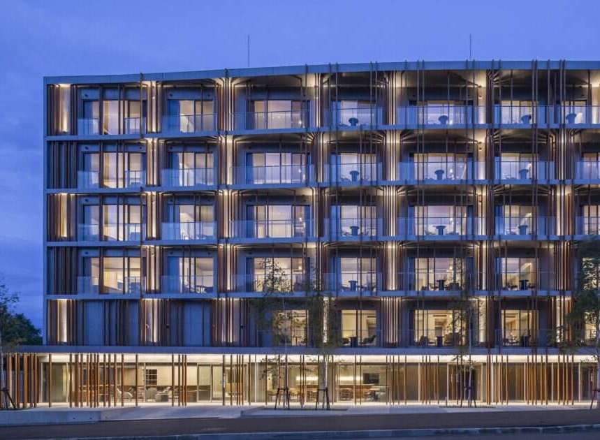 Experience modern living in this stunning multi-story building, featuring a unique facade with vertical wooden louvers and ample glass balconies.
