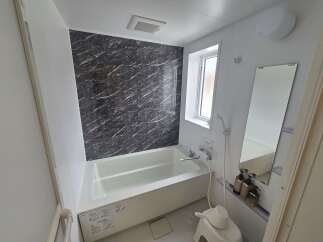 Experience modern comfort in this well-appointed bathroom, featuring a sleek bathtub with a striking dark marble-patterned accent wall.