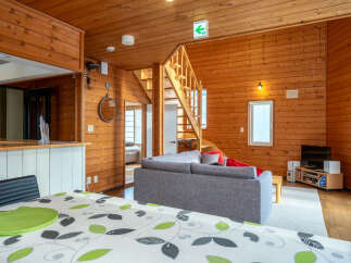 Experience rustic charm in this cozy wooden cabin living space, featuring a comfortable grey sofa and a dining area with a patterned tablecloth.