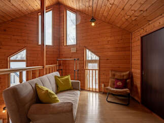 Experience cozy living in this charming wooden cabin featuring a comfortable sofa and accent pillows, perfect for relaxing.