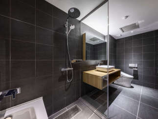Experience modern luxury in this sleek bathroom featuring dark tiled walls and a spacious walk-in shower with a rainfall showerhead.