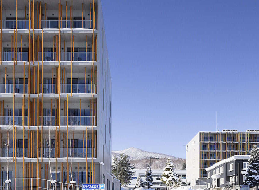 Experience modern living in this multi-story apartment building, featuring a striking facade with vertical wooden accents and glass balconies.
