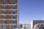 Experience modern living in this multi-story apartment building, featuring a striking facade with vertical wooden accents and glass balconies.