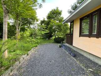 Discover this charming property featuring a gravel pathway leading to a cozy home with a light yellow exterior and dark brown trim windows.