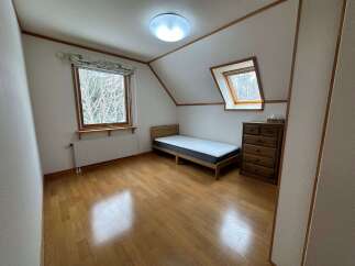 Discover this charming attic bedroom featuring a cozy single bed and a wooden dresser, perfect for a minimalist retreat.