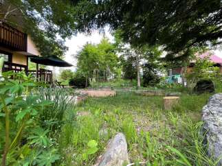 Discover a charming property nestled amidst lush greenery, featuring a welcoming house with a wooden balcony and an adjacent garden area.
