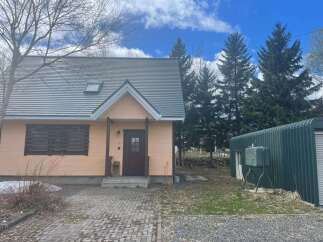 Charming peach-colored house with a dark brown door and a grey roof, featuring a unique slatted window covering.