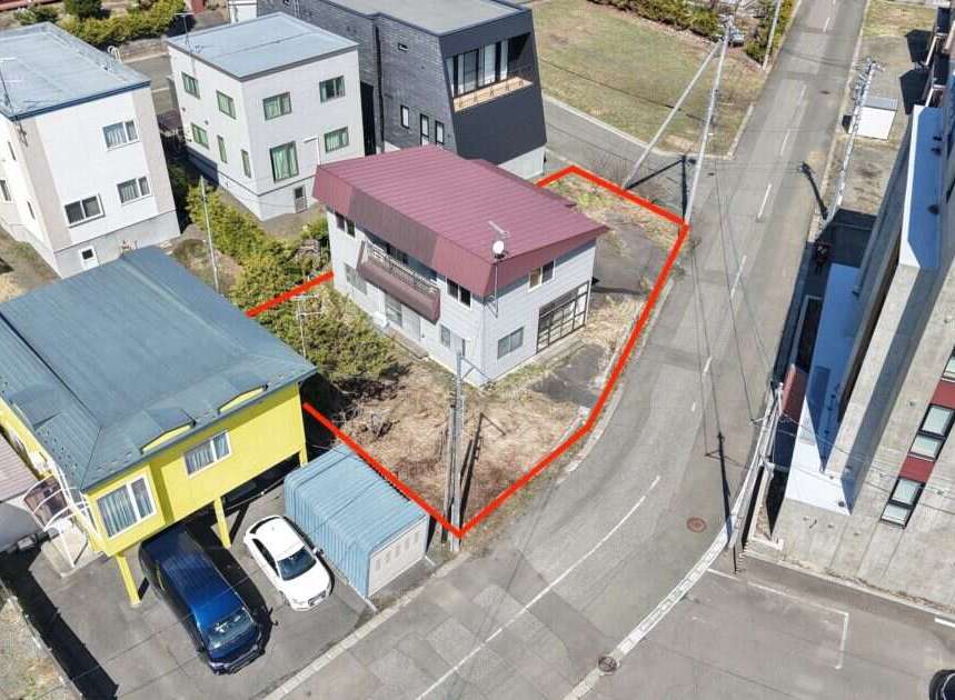 This aerial view showcases a residential property with a light gray exterior and a maroon roof, outlined by a red boundary.