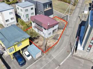 This aerial view showcases a residential property with a light gray exterior and a maroon roof, outlined by a red boundary.