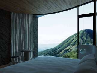 Experience breathtaking mountain views from this luxurious bedroom, featuring a curved floor-to-ceiling window that immerses you in nature.
