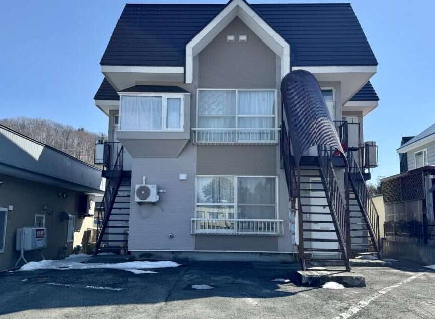 Discover this charming multi-story apartment building, featuring a modern gray and beige exterior with a dark pitched roof.