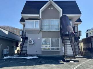Discover this charming multi-story apartment building, featuring a modern gray and beige exterior with a dark pitched roof.