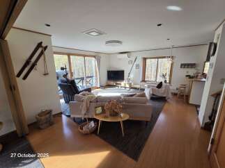 Experience cozy living in this inviting living room, featuring a comfortable sofa and a large window offering scenic views of autumn foliage.