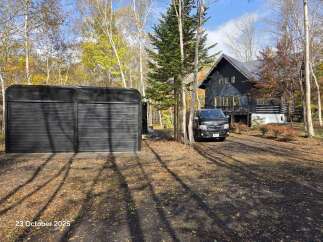 Discover this charming property nestled amidst a vibrant autumn forest, featuring a modern dark-colored house with a spacious deck and a detached garage.