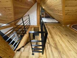 Experience rustic charm and modern comfort in this unique loft space, featuring exposed wooden beams and a sleek black metal railing system.