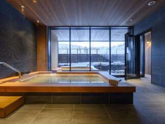 Experience ultimate relaxation in this luxurious indoor hot spring, featuring a spacious wooden-decked tub with ambient lighting.