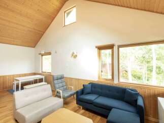 Experience cozy living in this charming room featuring a vaulted wood-paneled ceiling and abundant natural light from large windows.