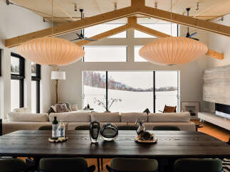 Experience luxurious living in this stunning open-concept dining and living area, featuring a vaulted ceiling with exposed wooden beams and two iconic Nelson bubble lamps.
