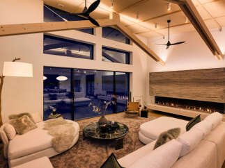 Experience modern luxury in this stunning living room, featuring a dramatic double-height ceiling with exposed wooden beams and sleek ceiling fans.