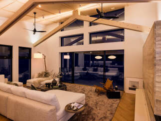 Experience modern luxury in this stunning living room featuring a soaring vaulted ceiling with exposed wooden beams and sleek ceiling fans.