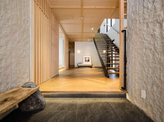 Experience the serene beauty of this entryway, featuring a unique wooden bench supported by natural stones and a striking textured stone wall.