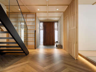 Experience modern Japanese living in this stunning entryway, featuring a sleek black staircase with glass railings and warm, herringbone wood flooring.