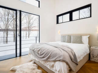 Experience modern luxury in this serene bedroom featuring expansive floor-to-ceiling windows that offer breathtaking winter landscape views.