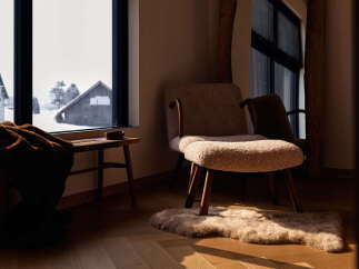 Experience cozy living with this inviting interior featuring a plush armchair and a warm, faux fur throw draped over a wooden bench.