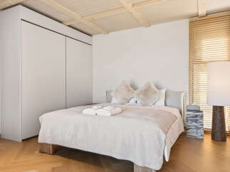 Experience ultimate comfort in this serene bedroom, featuring a plush bed adorned with soft, inviting linens and decorative pillows.