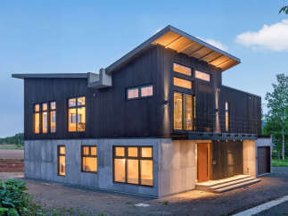 Experience modern living in this striking architectural home, featuring a dark wood exterior and a robust concrete base.