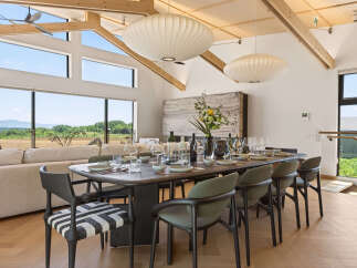 Experience modern luxury in this stunning dining room, featuring a large wooden table set for a feast and surrounded by elegant chairs.