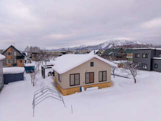 Experience winter charm in this snow-covered residential area, featuring a cozy single-family home with a light-colored exterior and a bright yellow foundation.