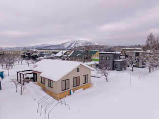 Experience winter living in this charming snow-covered neighborhood, featuring a cozy home with a bright yellow base and a snow-laden roof.