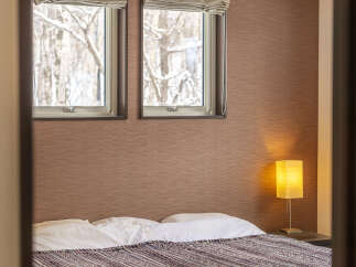 Experience cozy winter views from this charming bedroom, featuring two large windows overlooking a snow-covered forest.