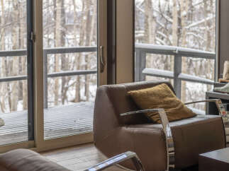 Experience cozy living with this inviting leather armchair, perfect for relaxing by the large windows overlooking a serene winter landscape.