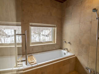 Indulge in a relaxing soak with a view in this luxurious bathroom, featuring a deep soaking tub positioned perfectly by a large window overlooking a serene winter landscape.