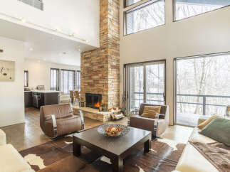 Experience luxurious living in this stunning open-concept great room, featuring a soaring stone fireplace and expansive windows that offer breathtaking views of the winter landscape.