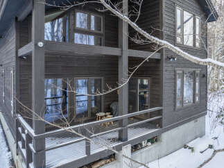 Experience the charm of this dark wood-sided home nestled in a snowy landscape.