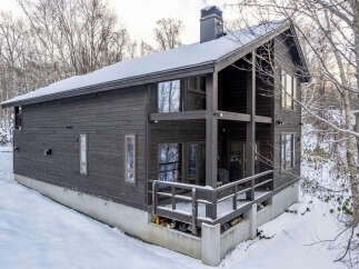 Experience the charm of this dark wood-sided home nestled in a snowy landscape.