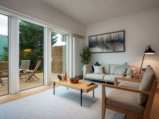 Experience modern living in this bright and airy living room, featuring a large sliding glass door that opens to a private deck and lush greenery.