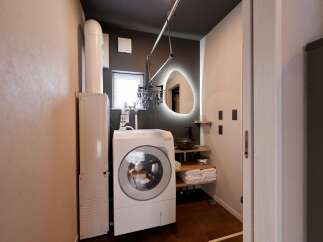 Discover modern convenience in this compact laundry and vanity area, featuring a front-load washing machine and a sleek sink with a unique illuminated mirror.