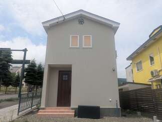 Discover this charming, narrow house featuring a light grey exterior and a dark brown front door with a small window pane.
