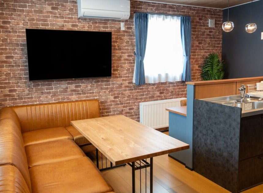 Experience modern living in this stylish apartment featuring a spacious L-shaped leather sofa and a rustic brick accent wall.