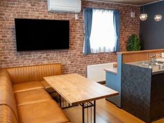 Experience modern living in this stylish apartment featuring a spacious L-shaped leather sofa and a rustic brick accent wall.